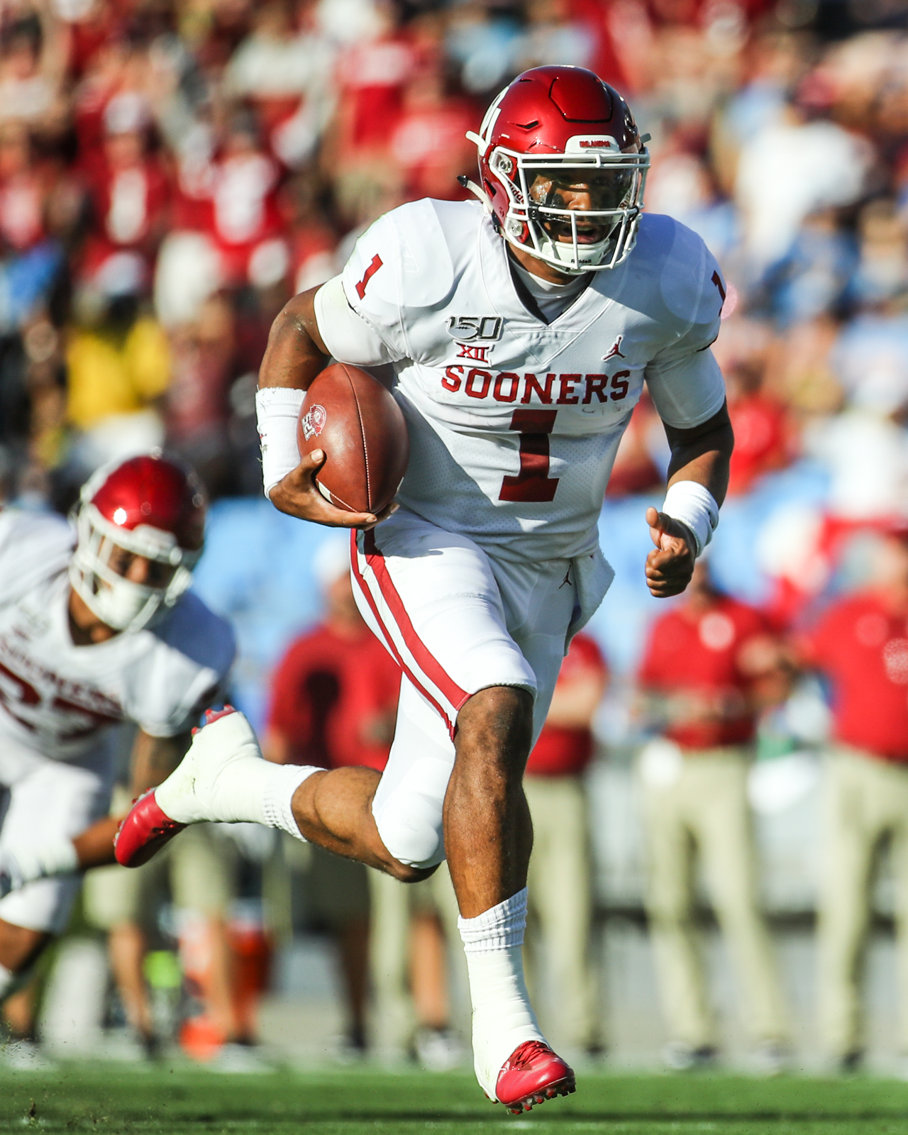 Jalen Hurts in a white Oklahoma Sooners football uniform running with the ball during a game.
