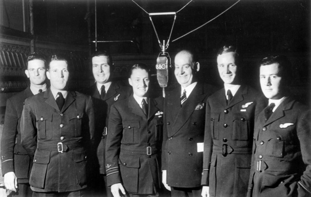 Seven men, some in RAAF uniforms, standing around a BBC microphone on a radio show set.