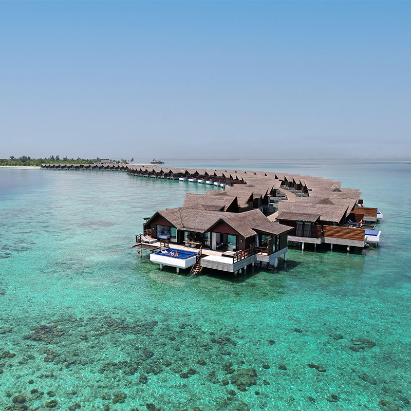 Overwater villas at a luxury beach resort surrounded by clear turquoise water in the Maldives.