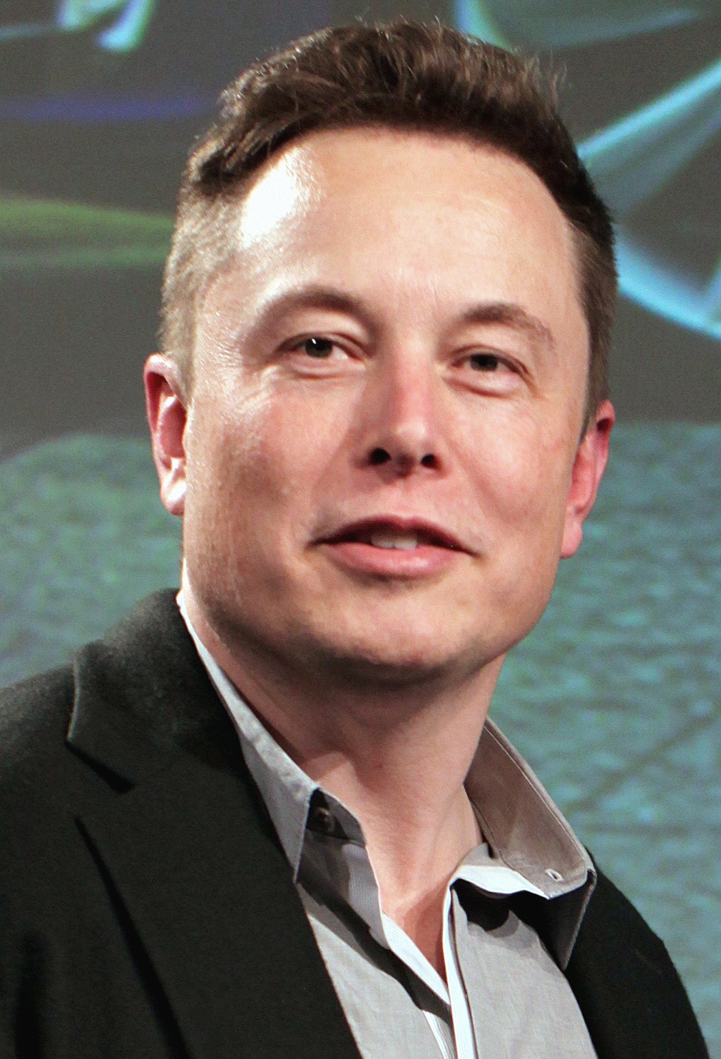 Close-up photo of Elon Musk wearing a light gray shirt and black jacket at the 2015 Tesla Motors Annual Meeting.