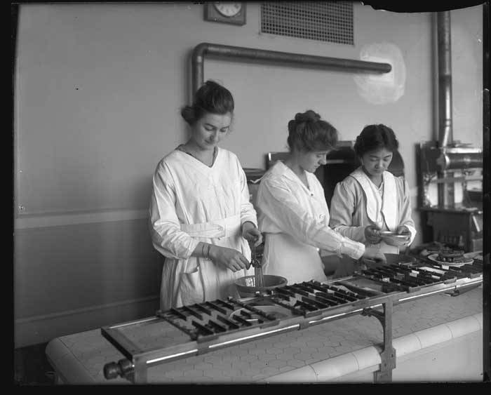 Three women in white dresses preparing ingredients in a cooking class at the University of Washington around 1918.