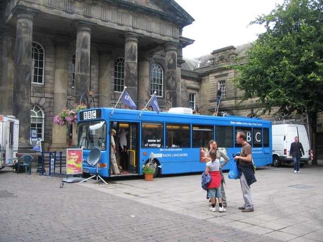A blue BBC Radio mobile studio parked outside Lancaster museum with people standing nearby.