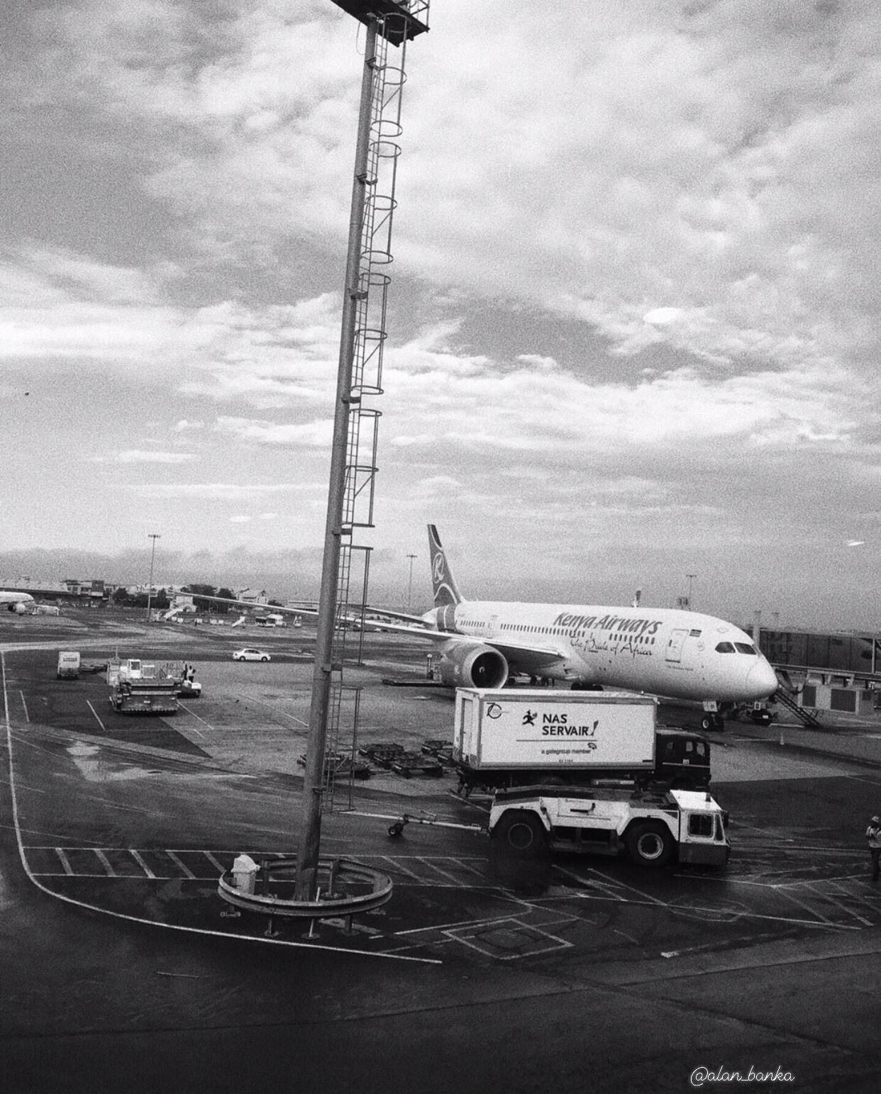 Kenya Airways airplane parked at Jomo Kenyatta International Airport with ground service vehicle nearby.