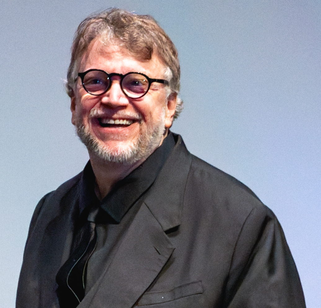 A man with glasses and gray hair wearing a black suit and smiling