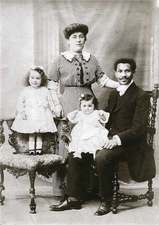 Black and white photograph of Joseph Laroche seated with a young child on his lap, standing next to his wife and another young child on a chair.