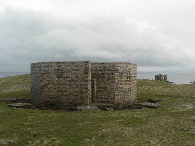 Brick circular wartime RAF radio location station structure on a grassy coastal area under cloudy sky