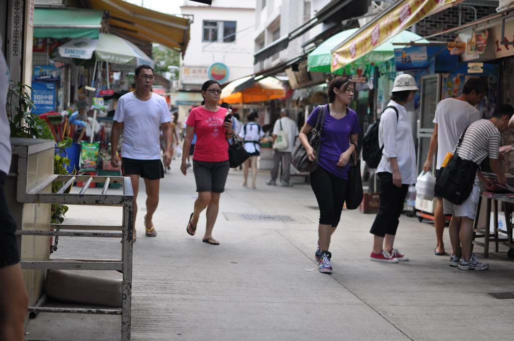 People walking and shopping along a street market with storefronts and awnings on Lamma Island.