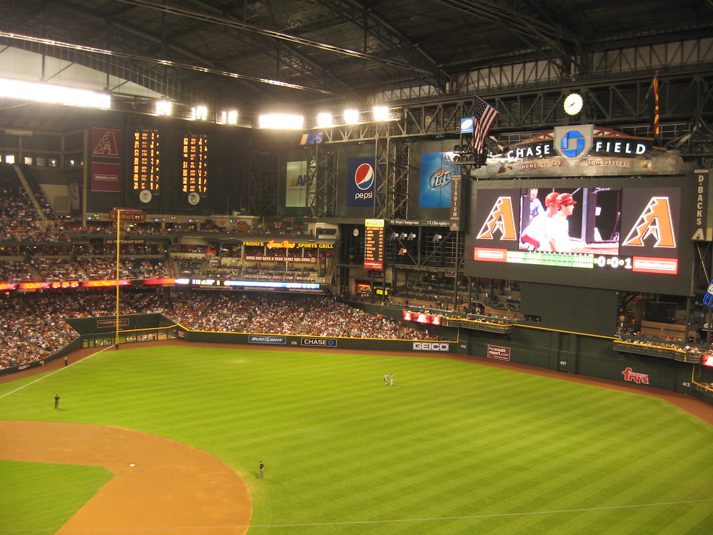 Wide view of a baseball stadium field with scoreboard showing Arizona Diamondbacks logos, crowd in stands, and players on the field