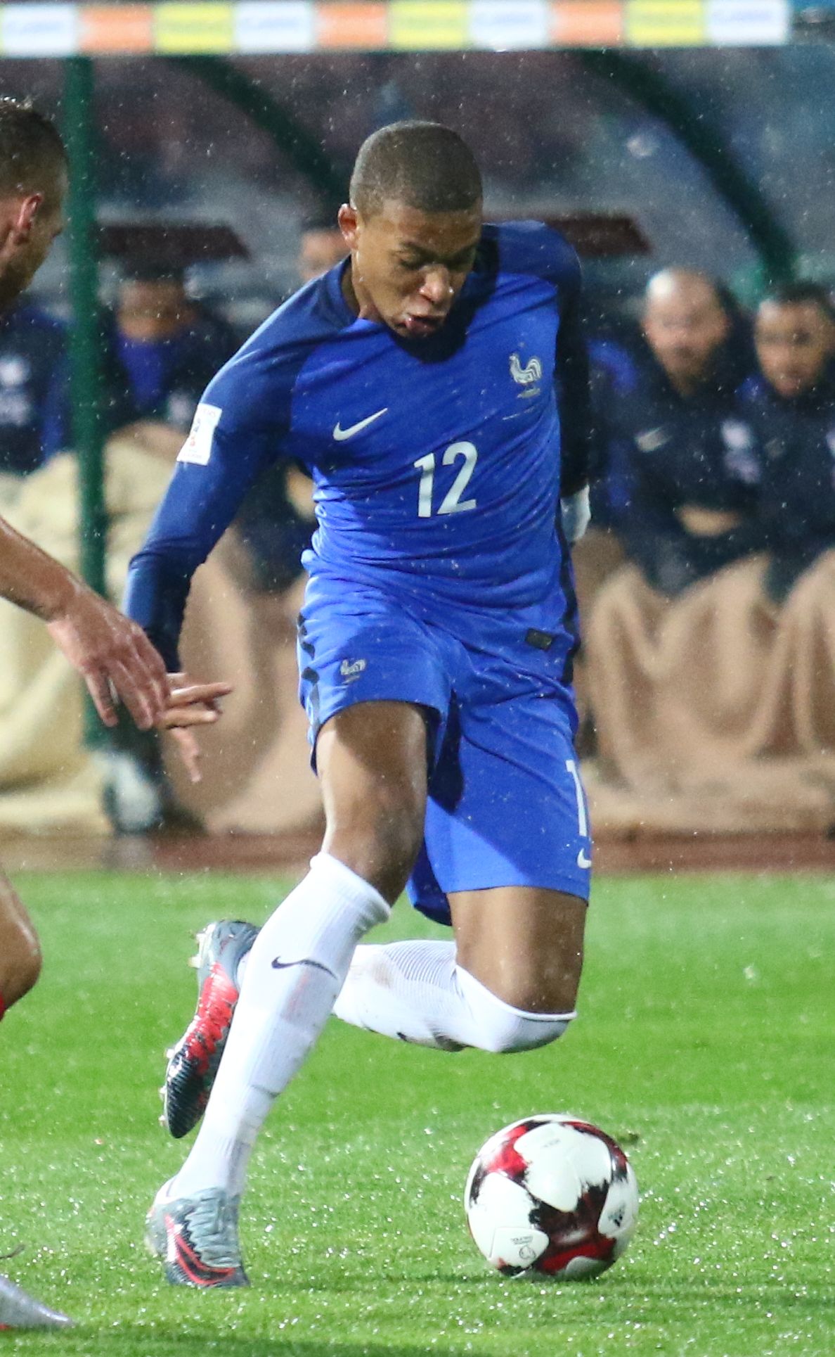 Football player in blue France national team kit, number 12, kicking a ball during a match.