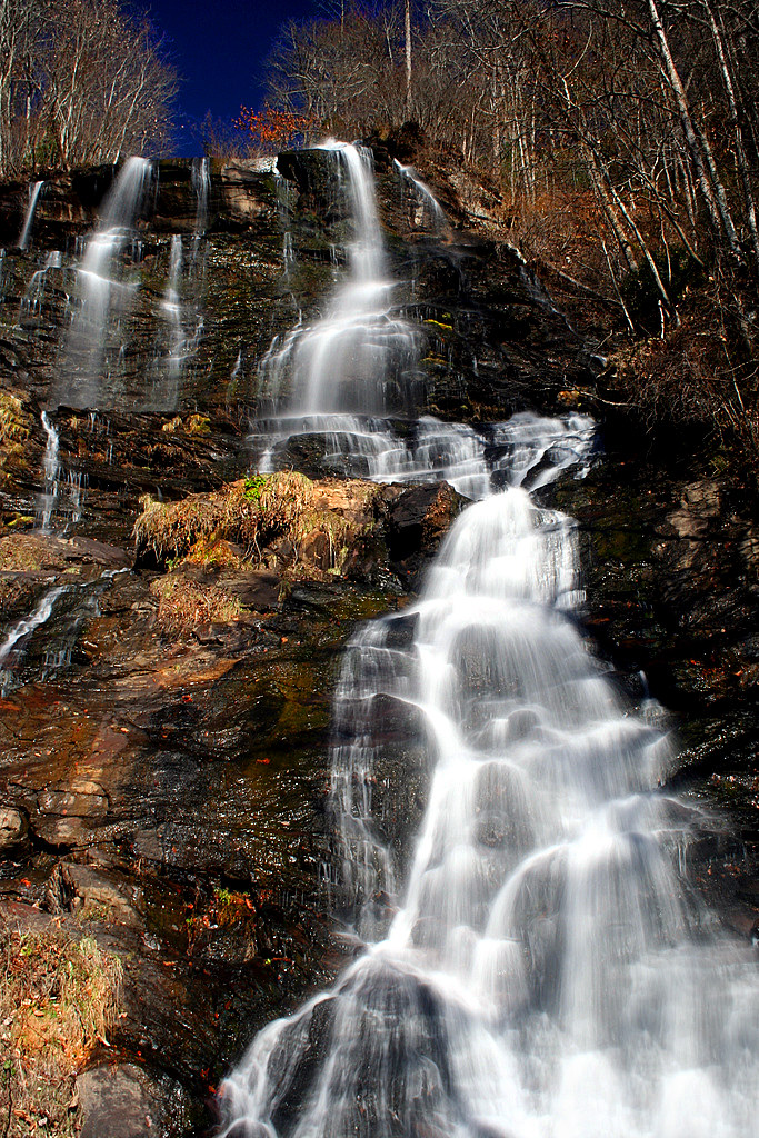 Waterfall cascading down rocky terrain surrounded by leafless trees under a deep blue sky.