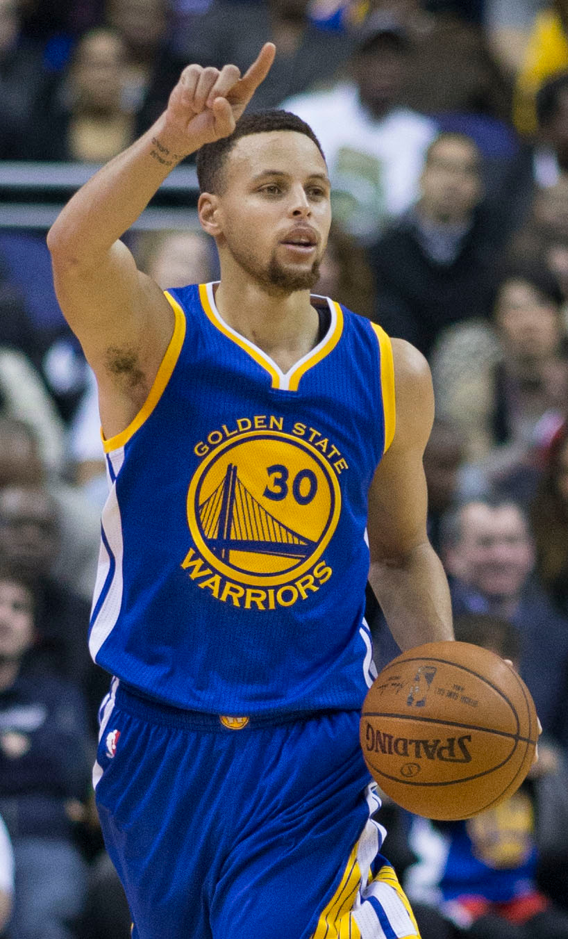 Basketball player in blue Golden State Warriors uniform number 30 dribbling basketball and raising index finger