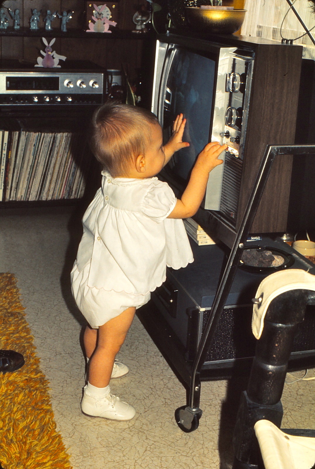 A toddler standing and touching an old-fashioned television set in a living room with a vintage interior.