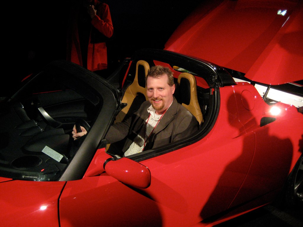 Man sitting inside a red Tesla Roadster car