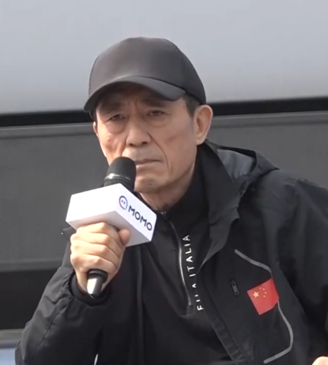 Man in black jacket and black cap holding a microphone