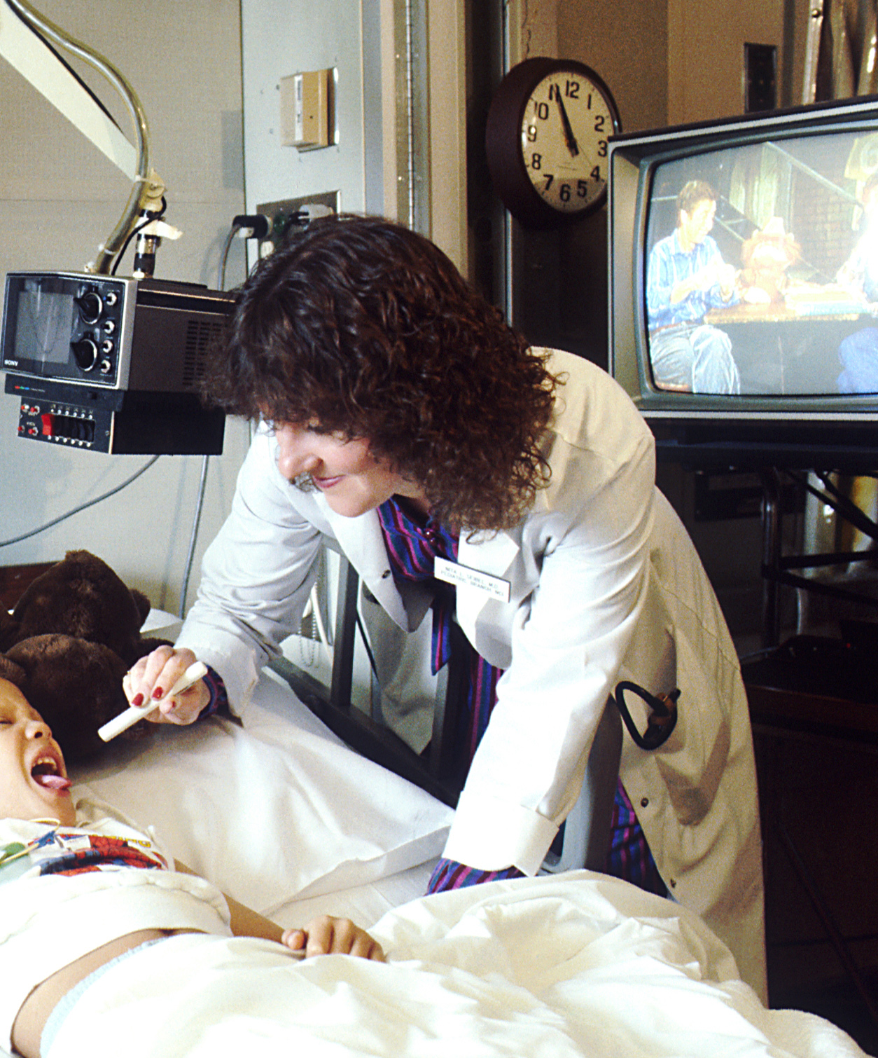 Doctor in white coat examining a child patient lying in hospital bed.