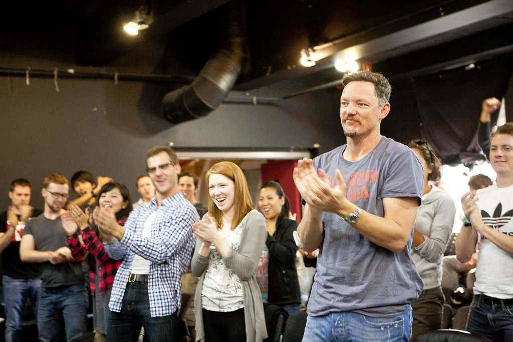 Man in a grey t-shirt clapping among a group of people in a workshop setting
