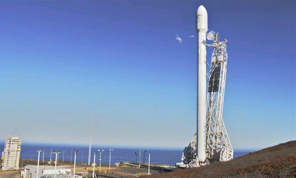 A SpaceX Falcon 9 rocket on a launch pad near the coast with clear blue sky.