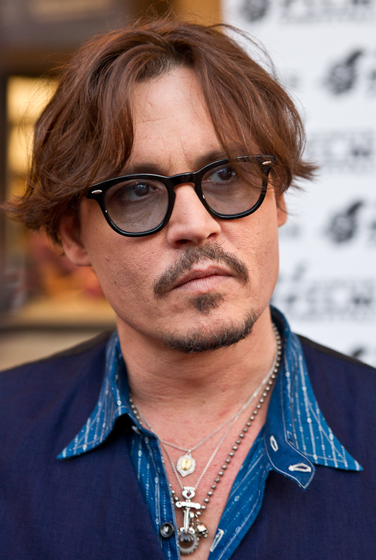 Close-up of Johnny Depp wearing glasses and layered necklaces at a public event.
