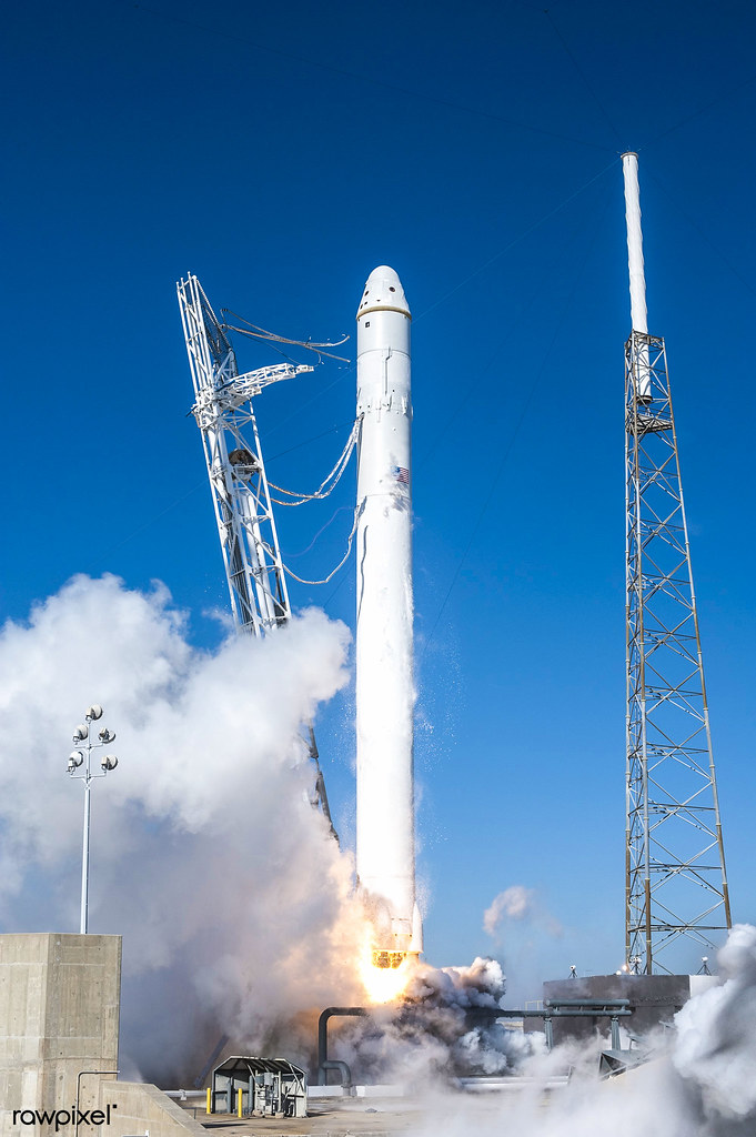 A SpaceX Falcon 9 rocket lifting off from a launch pad with smoke and flames at the base, clear blue sky background.