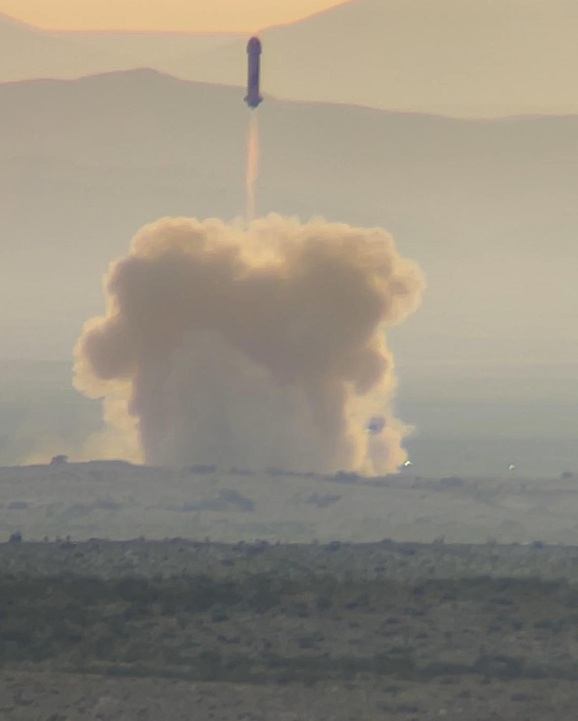 Blue Origin New Shepard rocket launching with smoke and flames, desert landscape in the foreground.