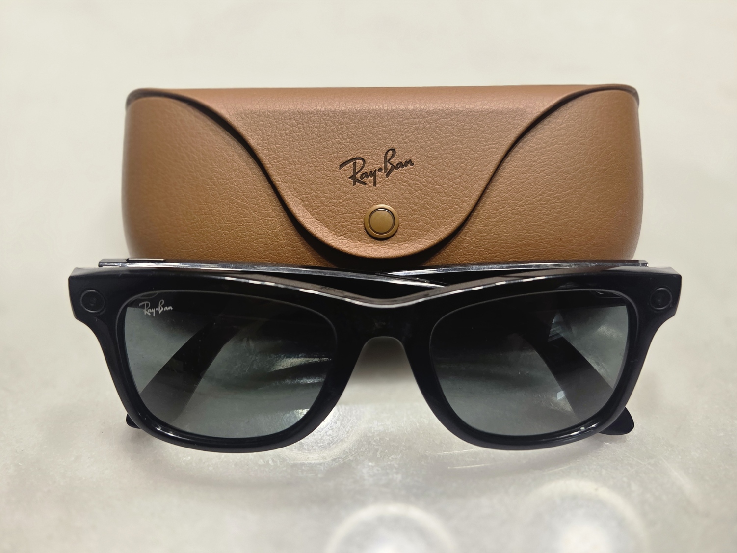 Ray-Ban Meta Gen 1 smart glasses in front of a brown Ray-Ban branded case on a light surface.