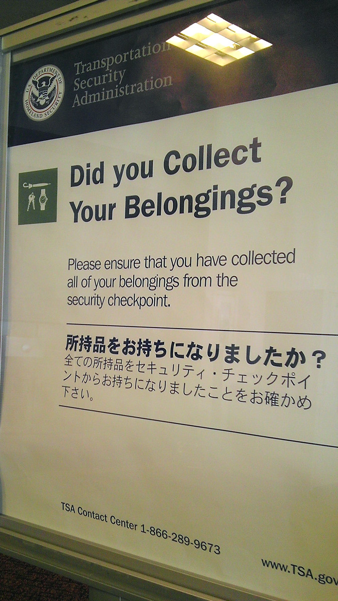 A sign at a TSA security checkpoint reminding travelers to collect their belongings, including text in English and Japanese, with TSA and Department of Homeland Security logos.