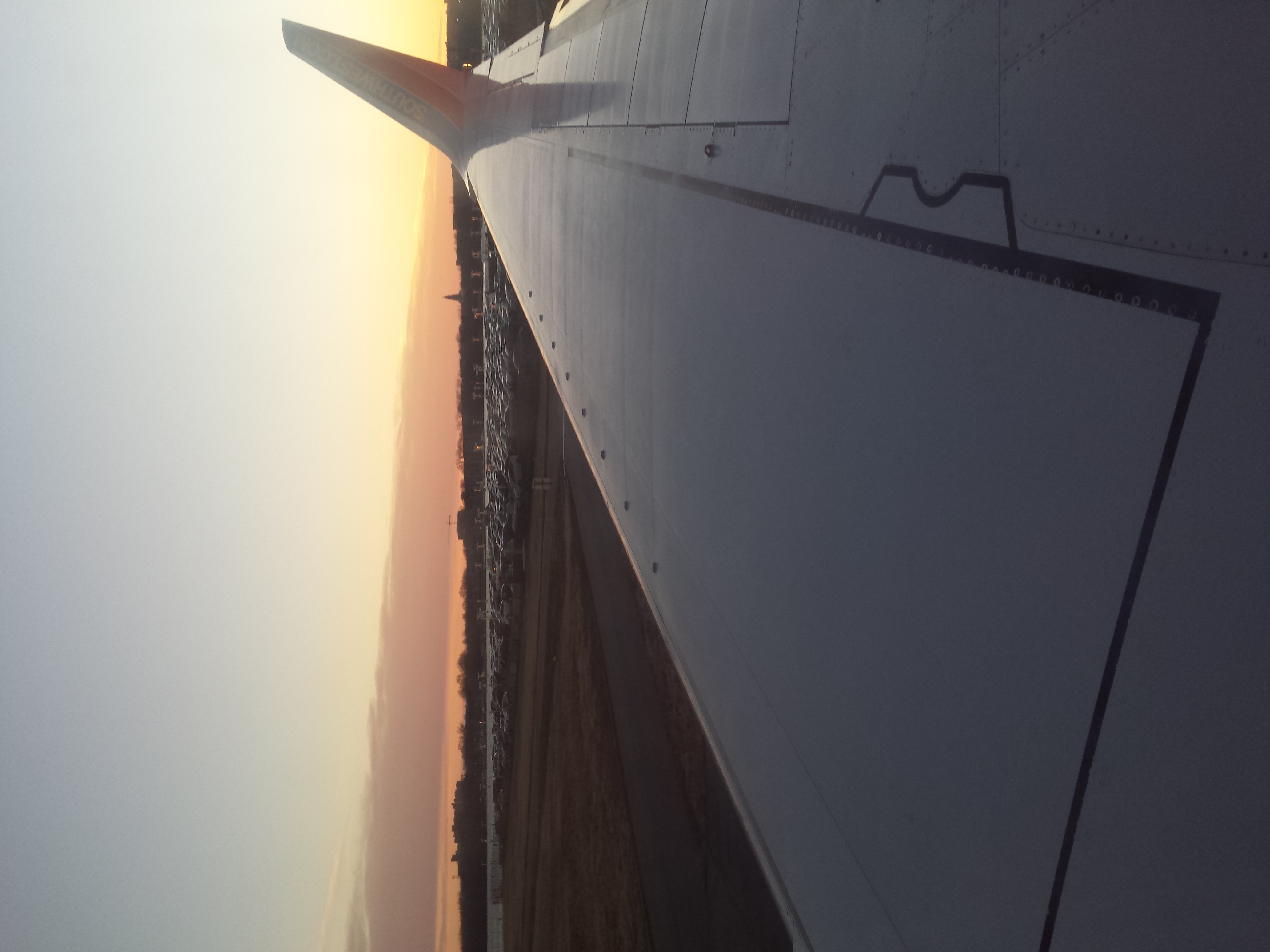 View of a commercial airplane wing and winglet with 'Southwest' text, taken at sunset from inside the aircraft on the starboard side.