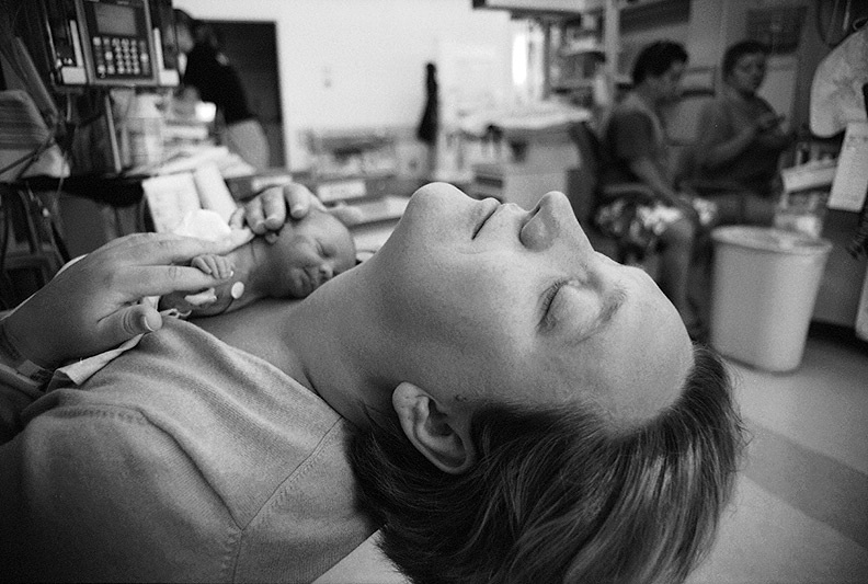 A mother lying down holding a tiny premature baby resting on her chest in a hospital environment.