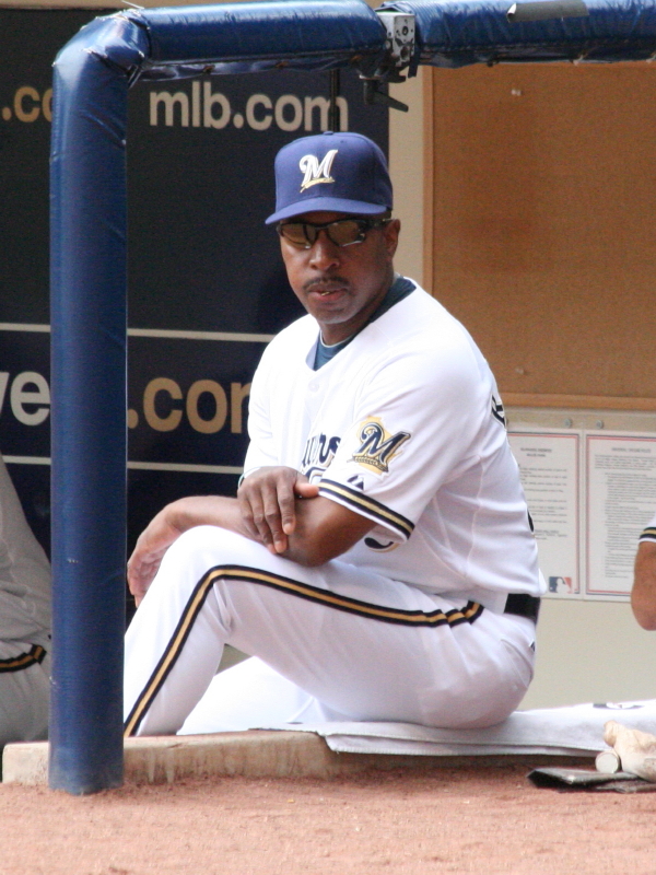 A man in a Milwaukee Brewers baseball uniform and cap sits in the dugout.